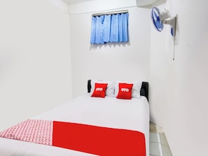 A hotel room with a bed, a window with blue curtains, a wall-mounted fan, and a red and white bedspread. - Mutiara Syariah 3 (Mataram)