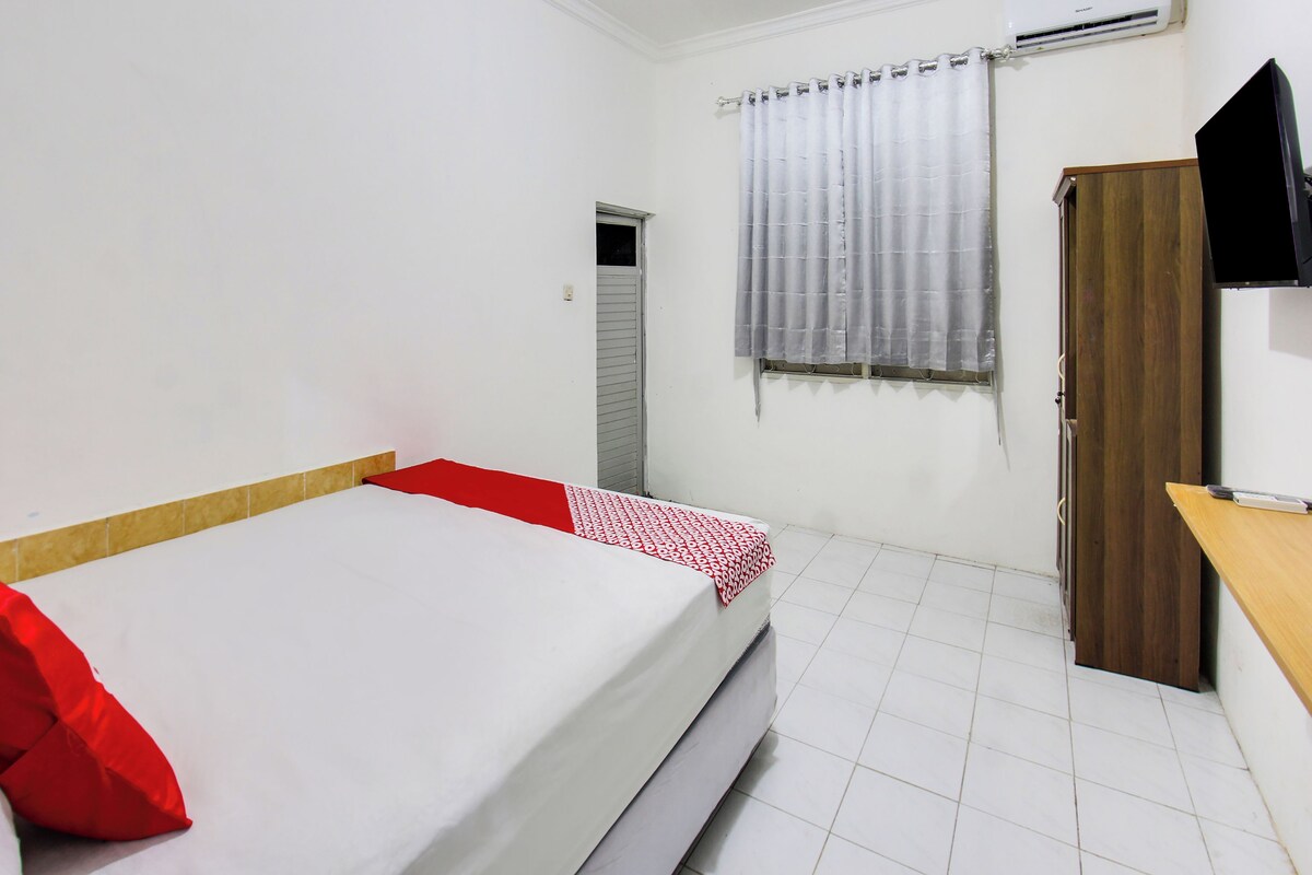 A room with a bed, a wooden desk, a television, and an air conditioning unit.