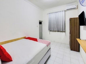 A room with a bed, a wooden desk, a television, and an air conditioning unit. - Mutiara Syariah 3 (Mataram)