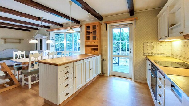 A kitchen with wooden cabinets, a central island, and a dining area with chairs.