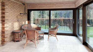 A room with wicker furniture, a brick wall, and a large sliding glass door leading to a garden.