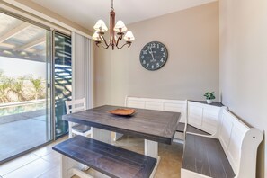 A dining area with a dark wooden table and bench, a chandelier, and a wall clock.