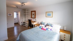 Een slaapkamer met een bed, een bureau en een stoel. Er is een kledingkast met planken en een spiegel.