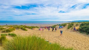 Een strand met mensen die wandelen en zitten in het zand, en duinen op de voorgrond.