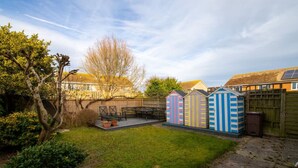 Een achtertuin met terras, houten schutting en kleurrijke tuinhuisjes.