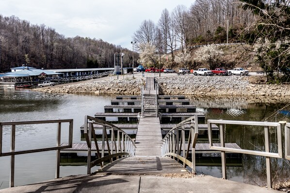 A wooden pier leading to a dock with a row of vehicles parked on the shore. - Tennessee Cabin w Hot Tub and Boating Access. (Tullahoma)