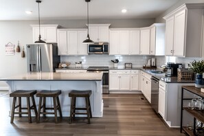 A modern kitchen with white cabinets, stainless steel appliances, and a large island with bar stools. - Tennessee Cabin w Hot Tub and Boating Access. (Tullahoma)