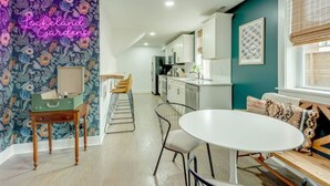 Una cocina moderna con armarios blancos, una zona de comedor con mesa y sillas blancas, y un letrero de neón en la pared.