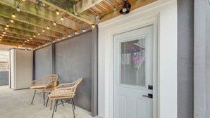Un espacio al aire libre techado con dos sillas de mimbre, una puerta blanca y luces colgantes en el techo.