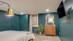 Un dormitorio con cama, cómoda, espejo y televisor en la pared.
