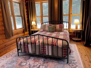 Un dormitorio de cabaña de madera con una estructura de cama metálica, un edredón estampado y dos lámparas de noche.