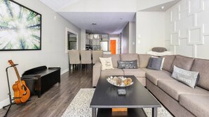 A modern living room with a sofa, coffee table, and a guitar. There is a dining area with chairs and a kitchen in the background. - Modern Ski-in Townhome with Hot Tub (Whistler)