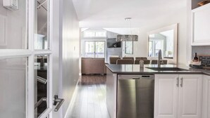 A modern kitchen with a dishwasher, a dining area with a glass table, and a sofa. - Modern Ski-in Townhome with Hot Tub (Whistler)