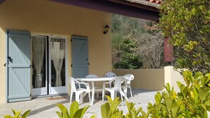 Une terrasse avec une table et des chaises, une porte-fenêtre coulissante et un luminaire fixé au mur.