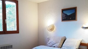 Une chambre à coucher comprenant un lit, une fenêtre, un tableau accroché au mur et un luminaire fixé au mur.