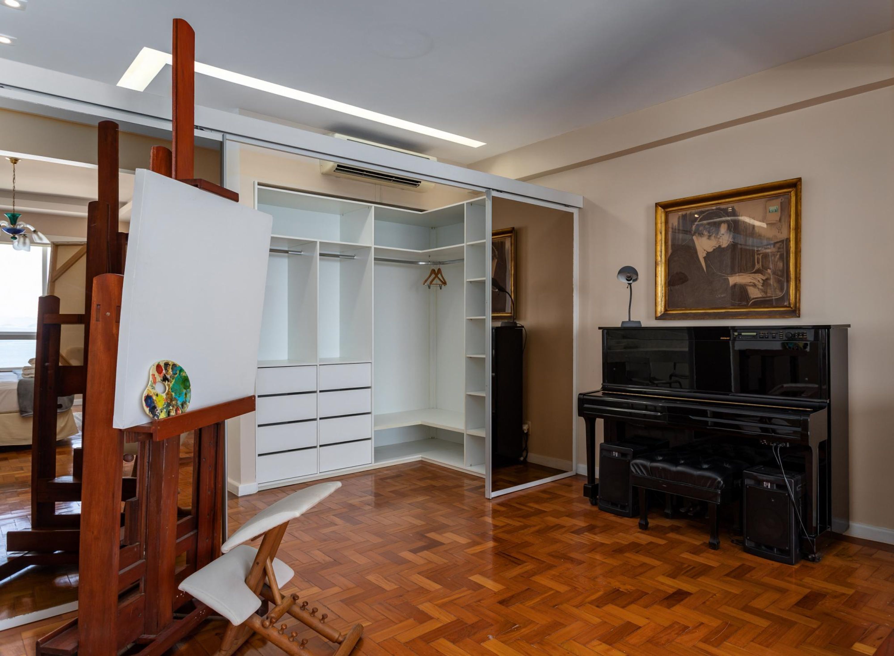 A spacious room with a wooden floor, a piano, a large white closet, and a painting on the wall.