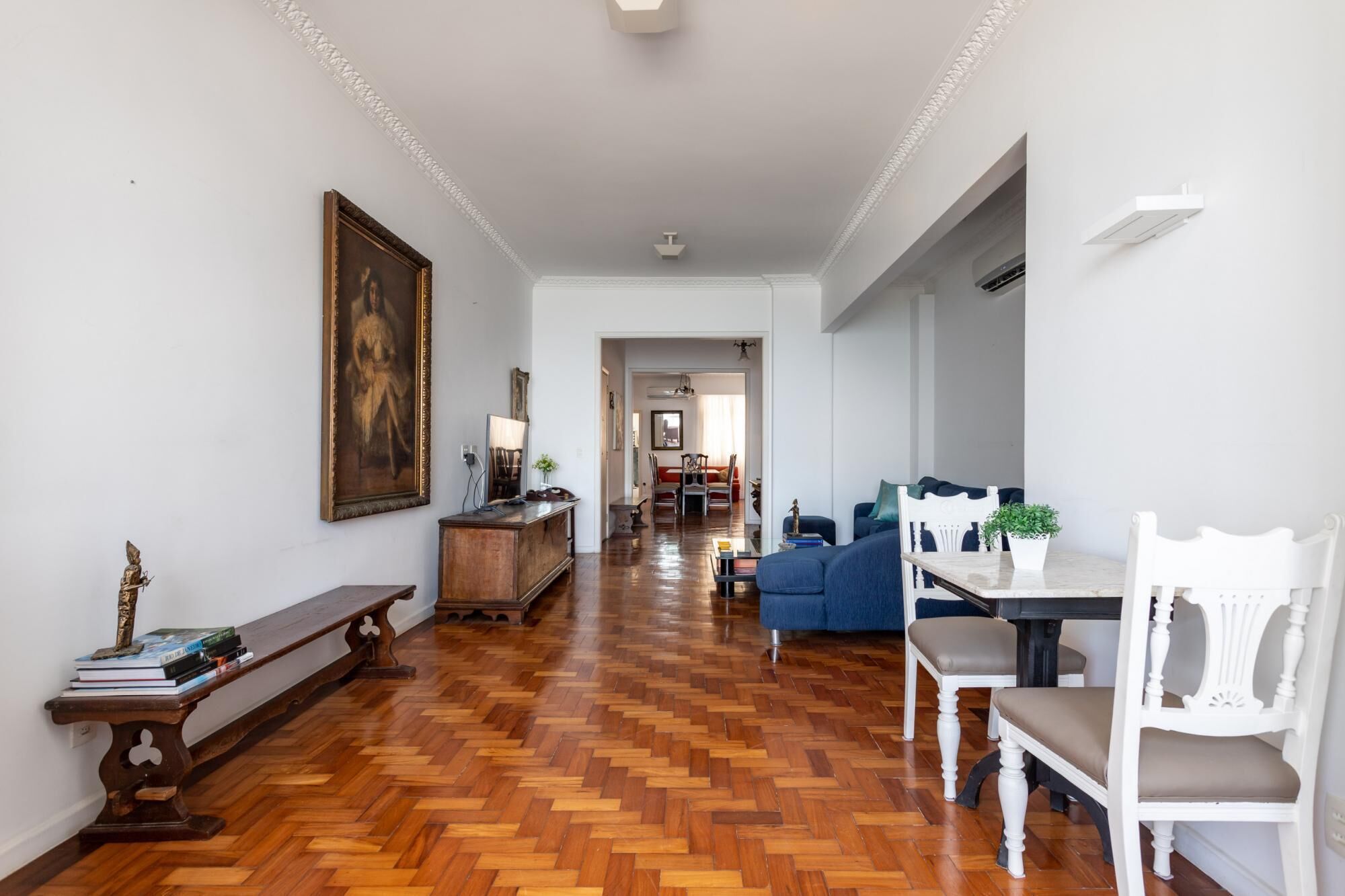A spacious living area with a wooden parquet floor, a dining table with chairs, a sofa, and a bench.