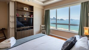 A hotel room with a bed, a television, a bookshelf, a window with a view of the beach, and a lamp. - A 2 Minutos de la Playa de Copacabana A801 (Rio de Janeiro)