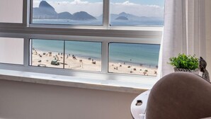 A room with a large window overlooking a beach, a small table with a plant, and a chair. - A 2 Minutos de la Playa de Copacabana A801 (Rio de Janeiro)
