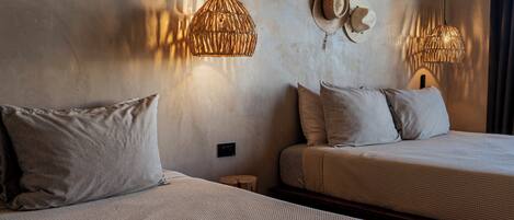 A hotel room with two beds, each with a textured bedspread and pillows. There are two wall-mounted lamps with a woven design.