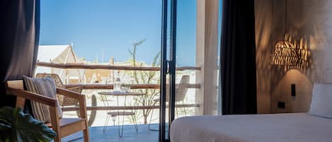 A bedroom with a bed, a chair, a table, and a view of the outdoors.