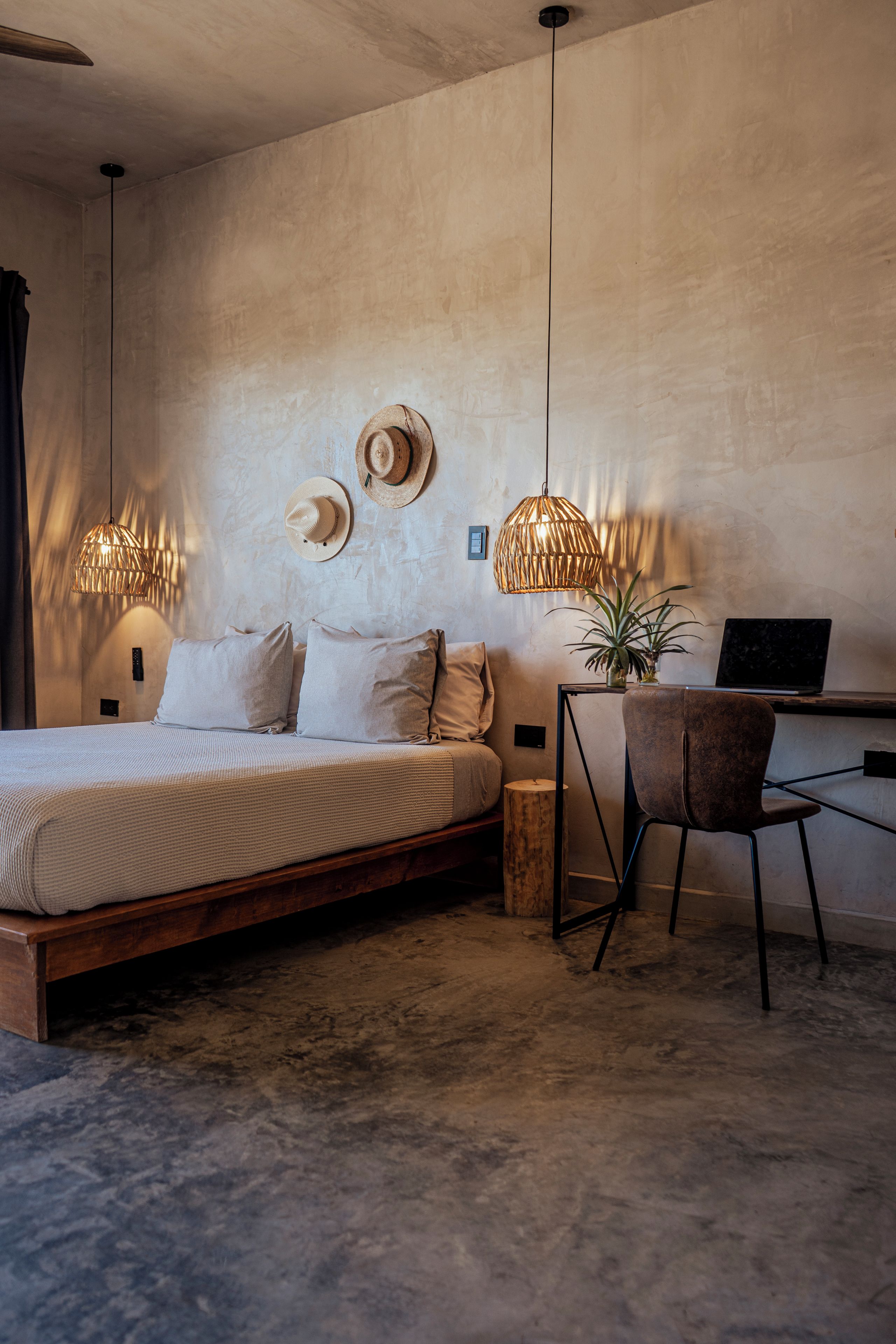 A bedroom with a bed, a desk, two lamps, and a potted plant.