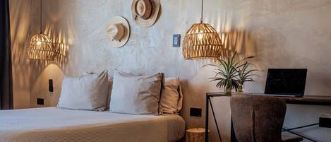 A bedroom with a bed, a desk, two lamps, and a potted plant.