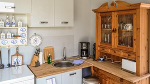 Eine Küche mit weißen Schränken, einem Holzschrank mit Glastüren, einer Kaffeemaschine und verschiedenen Küchenutensilien.