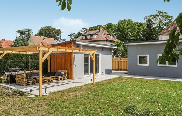 Een achtertuin met een houten pergola, een barbecueplek en een klein terras met een tafel en stoelen.