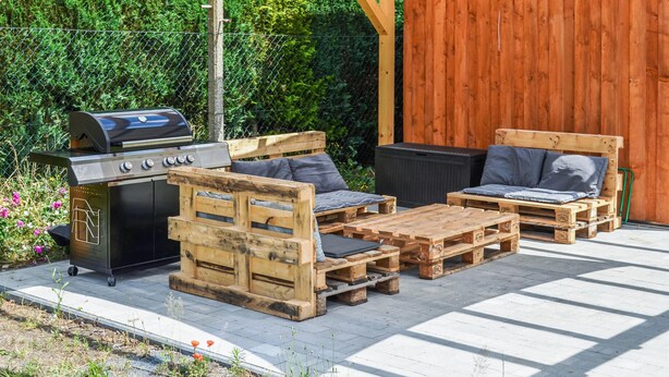 Eine Terrasse mit Grill, Holzmöbeln und einem Holenzaun.