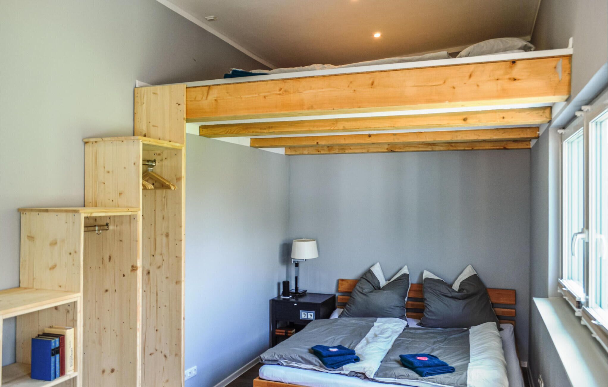 Una camera compatta con un letto a castello, un comodino con lampada e scaffalature in legno a muro.
