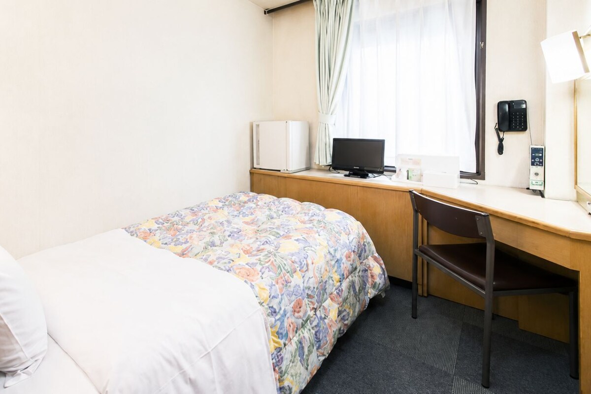 Een hotelkamer met een bed, een bureau, een stoel, een lamp, een telefoon en een raam met gordijnen.