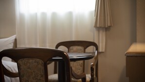 A room with two wooden chairs and a small table, a window with curtains, and a bedside table. - Business Hotel Toyo (Iwaki)