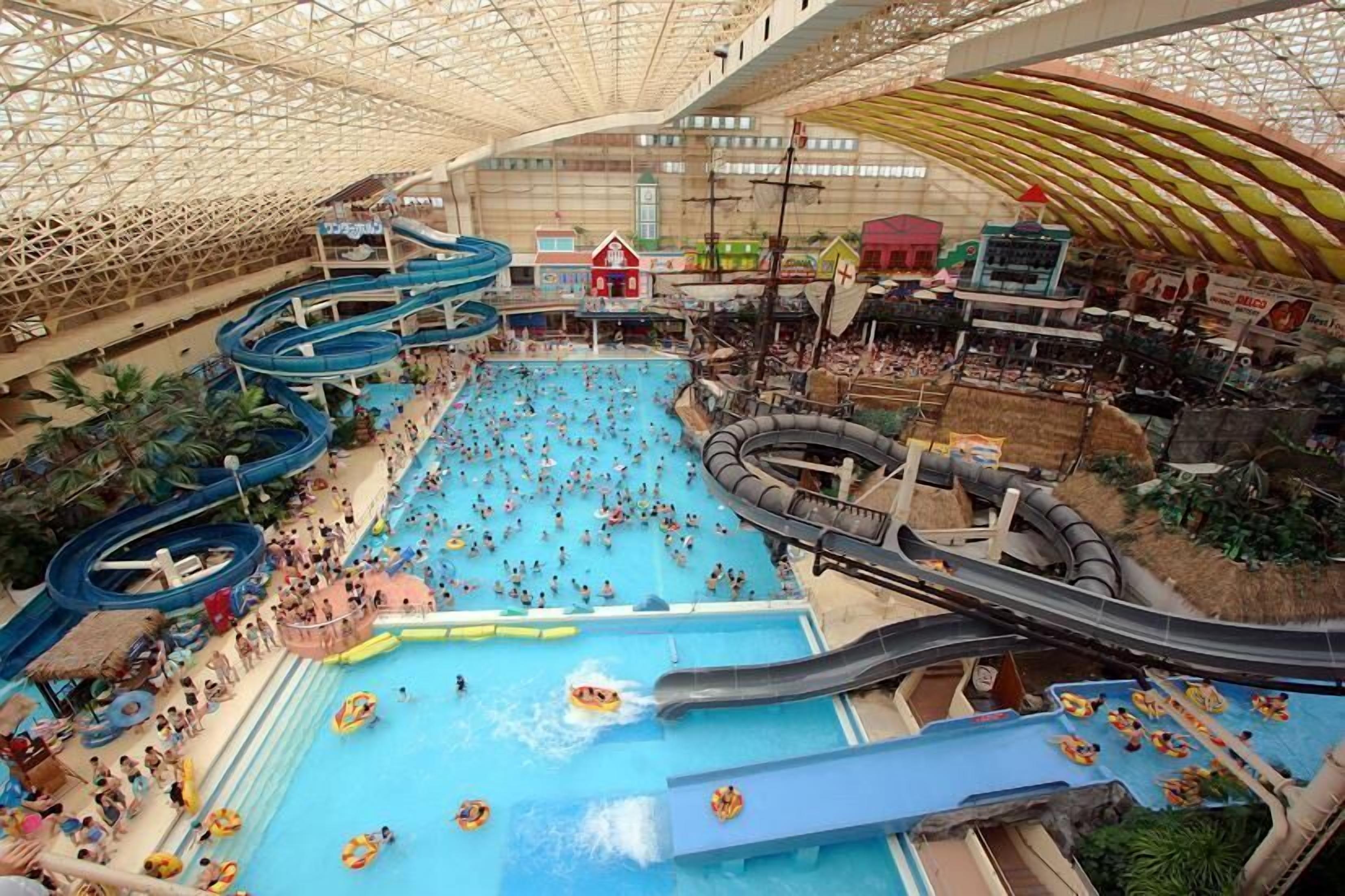 Um parque aquático interno com vários toboáguas e piscinas, rodeado por diversas lojas e atrações.