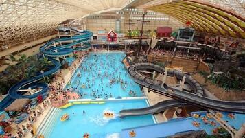 Um parque aquático interno com vários toboáguas e piscinas, rodeado por diversas lojas e atrações.