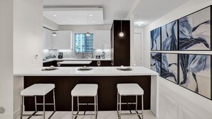 A modern kitchen with a central island, bar stools, and abstract art on the wall. - Fort Lauderdale Luxury Condo (Fort Lauderdale)