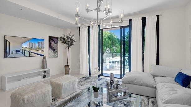 A modern living room with a glass coffee table, white sofas, a chandelier, and a large window with curtains. - Fort Lauderdale Luxury Condo (Fort Lauderdale)