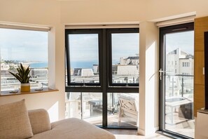 Enjoy a panoramic view of the city and sea from this room's large window, featuring a comfortable sofa and a minimalist design.
