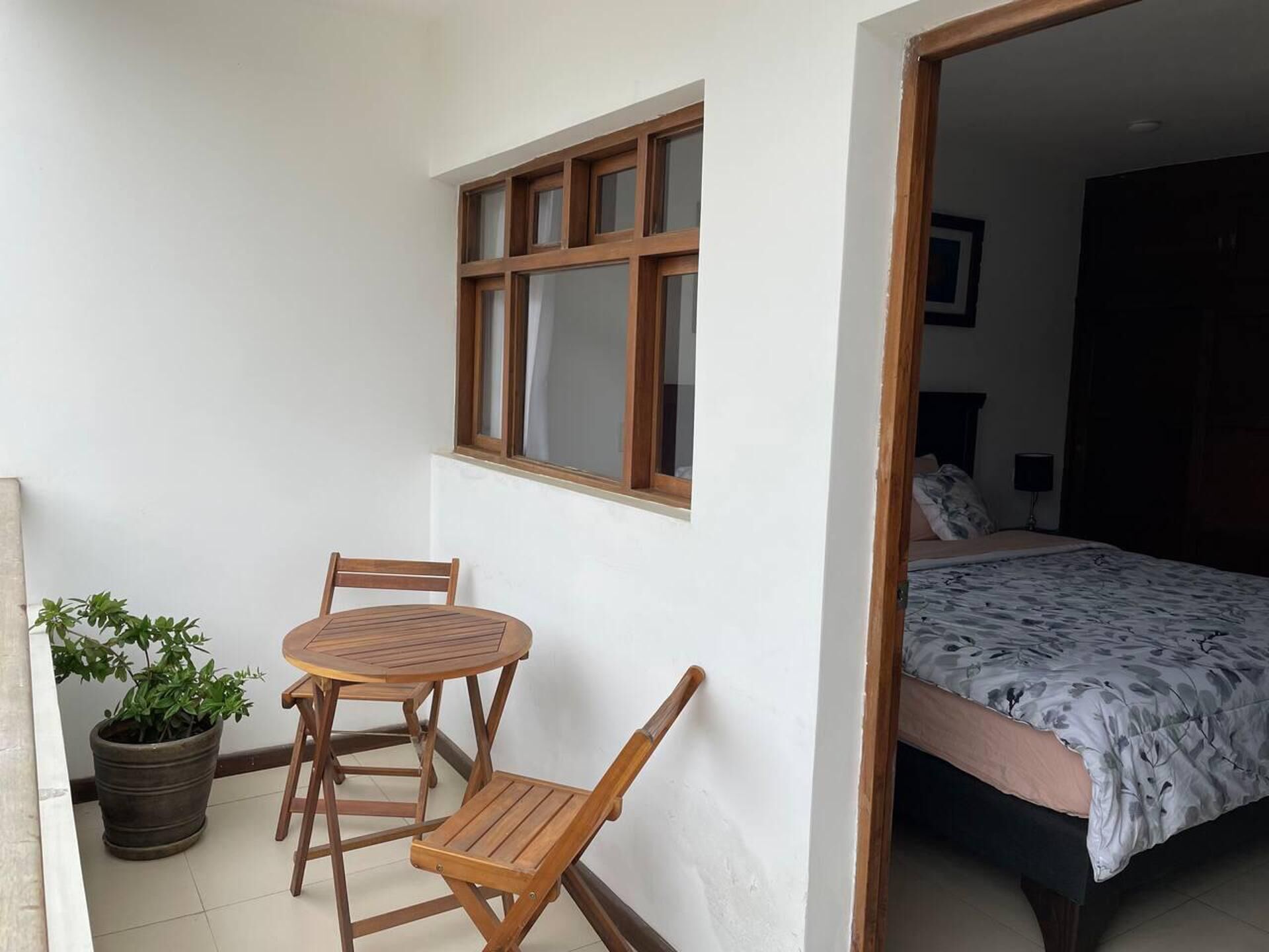 Une pièce avec un lit, une petite table avec des chaises, une plante en pot et une fenêtre.