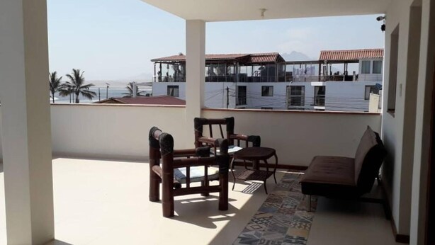 A balcony with a table and chairs, a patterned rug, and a view of buildings and palm trees. - Huanchacostudio/kingbed/balcony/tv/wifi (Huanchaco)