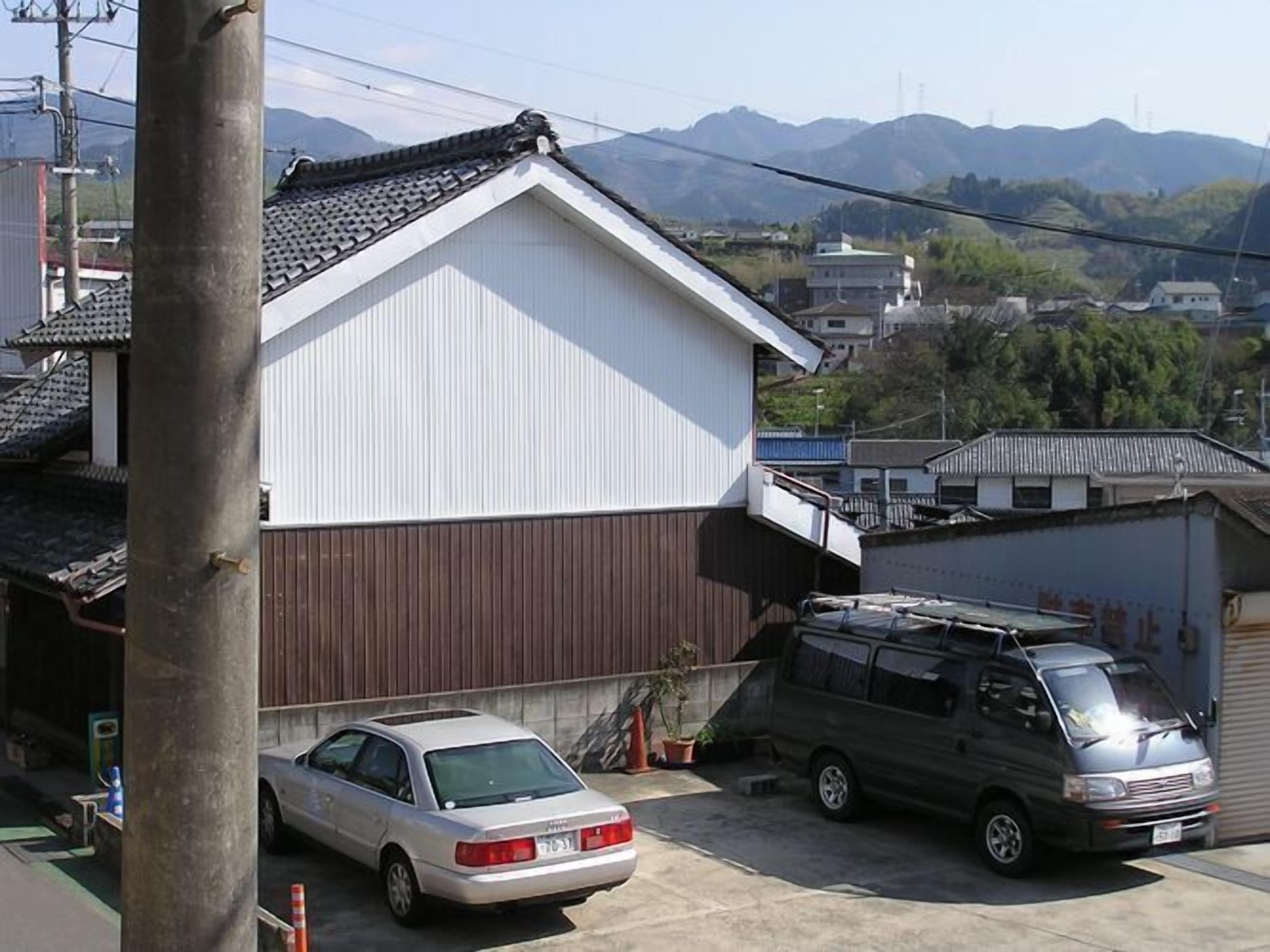 A residential area with a white building, a parked silver car, and a dark van.