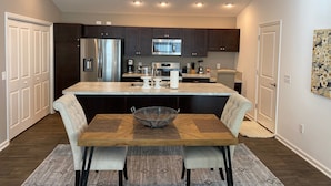 A modern kitchen with dark cabinets, stainless steel appliances, and a central island with a sink and stools. - 356 Hood Pl (Wildwood)