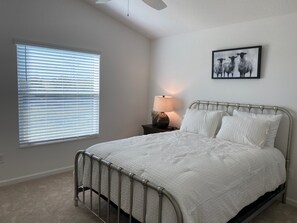 A bedroom with a metal bed frame, white bedding, a bedside lamp, a framed picture on the wall, and a window with blinds. - 356 Hood Pl (Wildwood)