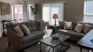 A living room with two grey sofas, a coffee table, and a lamp. There is a plant, a window with blinds, and a door leading outside. - 356 Hood Pl (Wildwood)