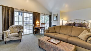A spacious living room with a large window, a sofa, a patterned ottoman, a vintage armchair, and a dining area with a table and chairs. - Cozy Portland Studio w/ Electric Fireplace (Portland)
