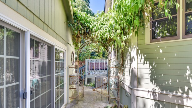 A narrow alleyway with a metal gate, a small garden area, and a building with a garage door. - Cozy Portland Studio w/ Electric Fireplace (Portland)