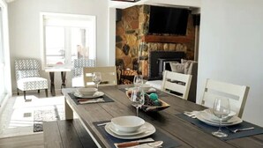 Un comedor con una larga mesa de madera dispuesta para cuatro personas, rodeada de sillas. Se ve una chimenea de piedra al fondo.