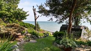 Un jardín tranquilo con vista al mar, que cuenta con un banco de madera, un cobertizo pequeño y una variedad de plantas.