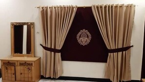 A room with a large mirror, a wooden cabinet, and beige curtains with a decorative central panel. - Hotel Royal Defence (Lahore)