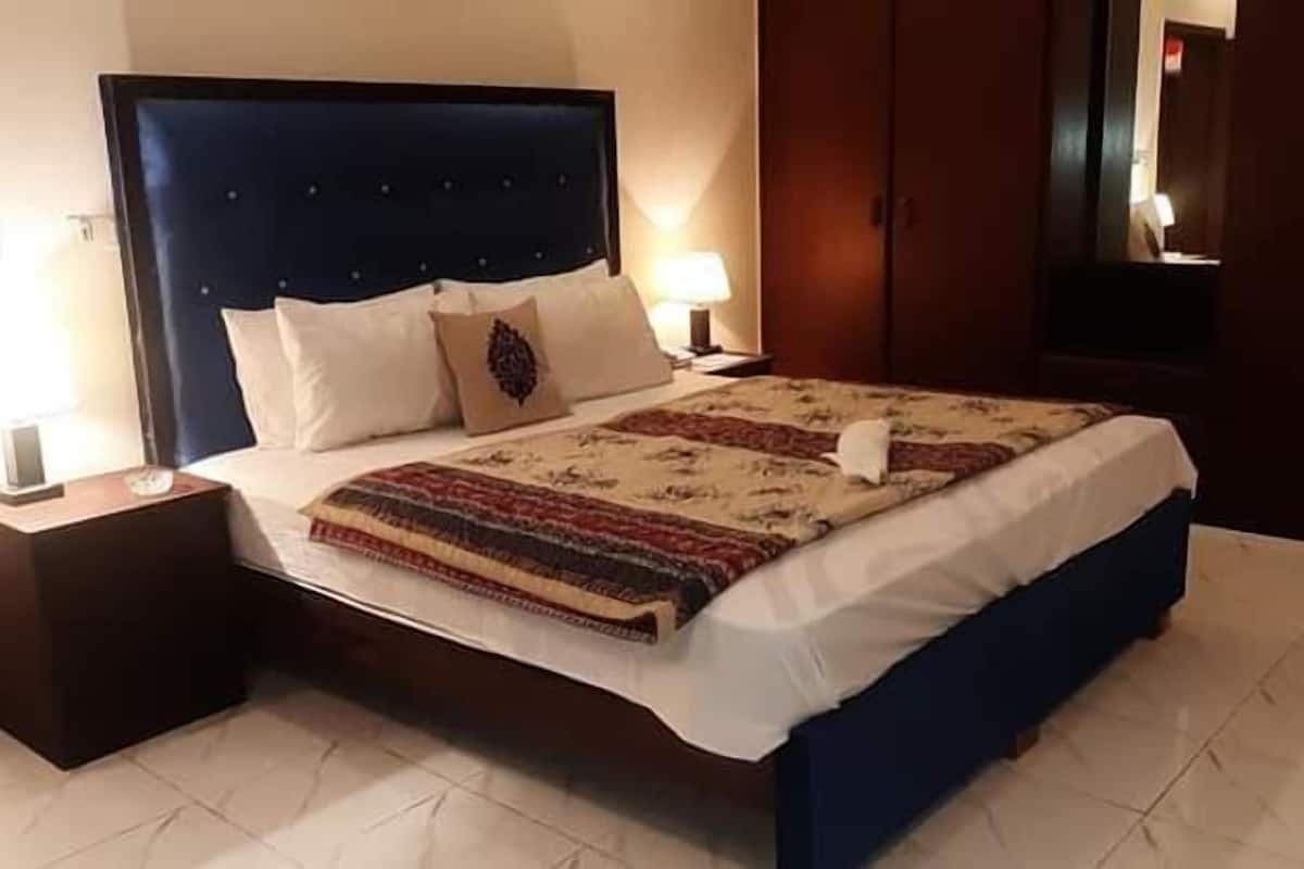 A hotel room with a large bed, two bedside tables, a nightstand, a wardrobe, and a mirror.